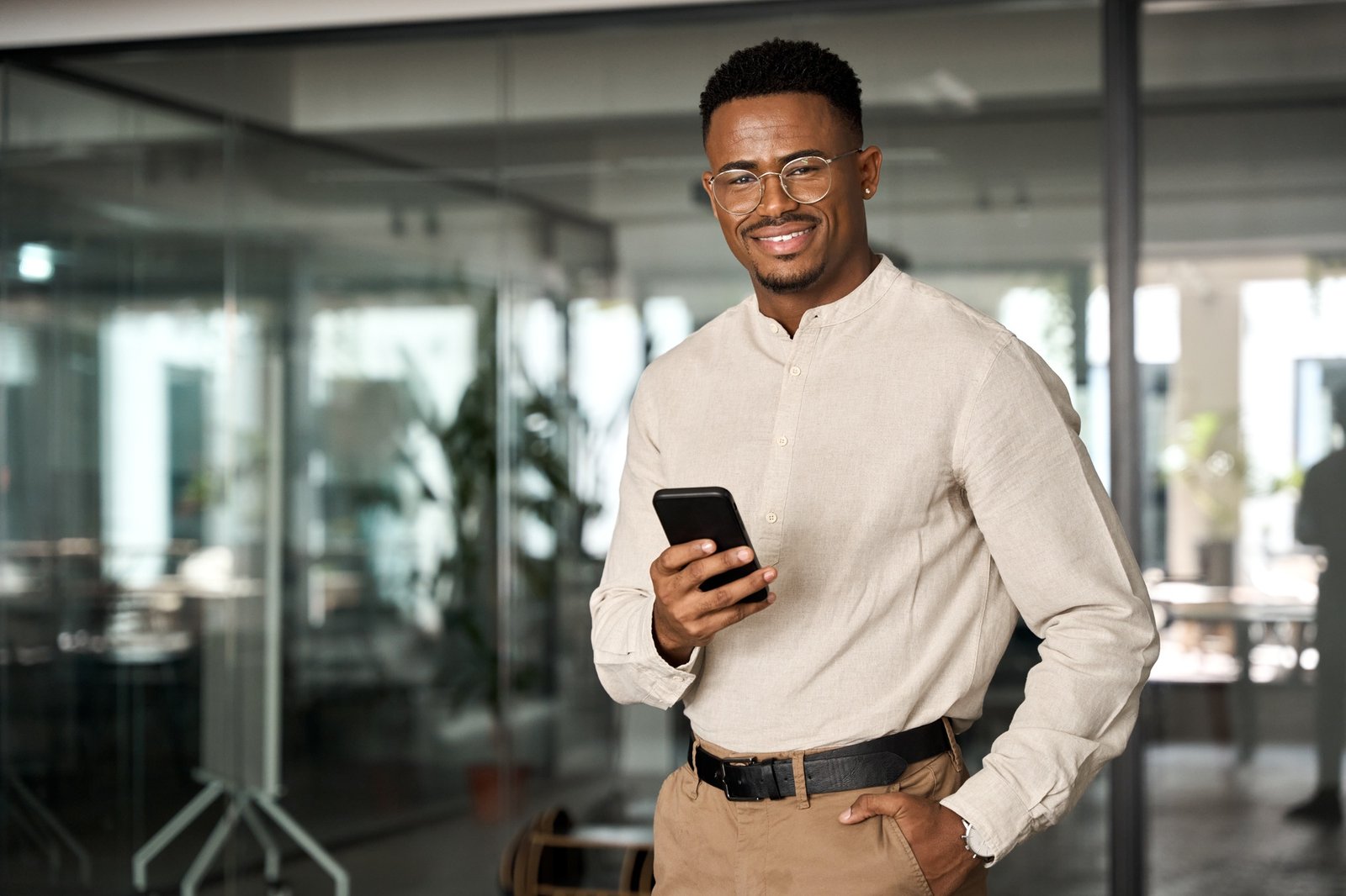 Happy professional African American business man standing in office using phone.